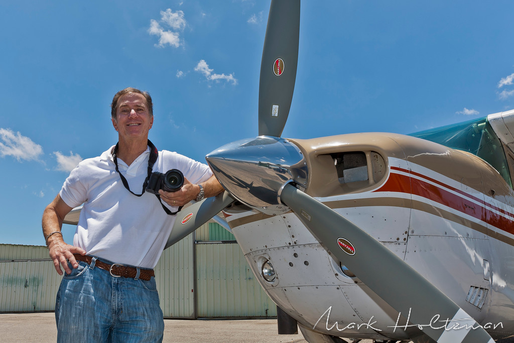 man standing next to a plane holding a camera
